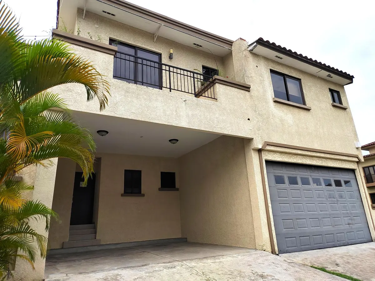 Front of a three-bedroom townhouse at Embassy Club in Clayton, with a two-storey stucco facade, a tile roof, a balcony and a grey garage door.