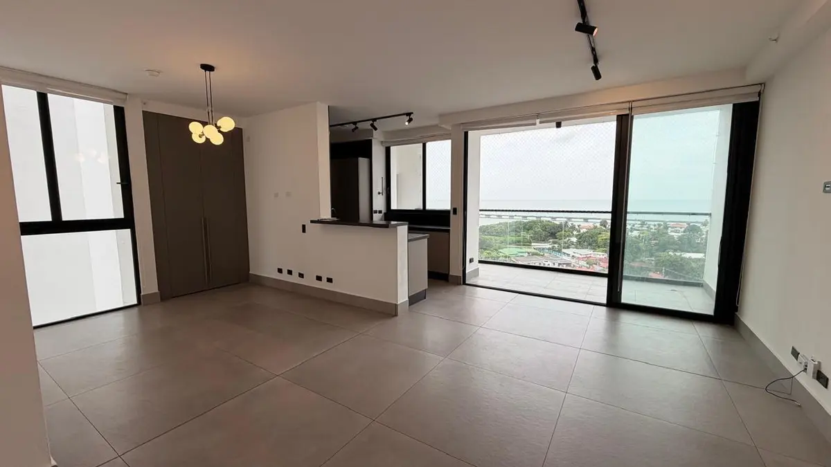 Living and dining area of a two-bedroom apartment at PH Victory Wellness in San Francisco, with grey tile floors, track lighting and glass doors to the balcony.