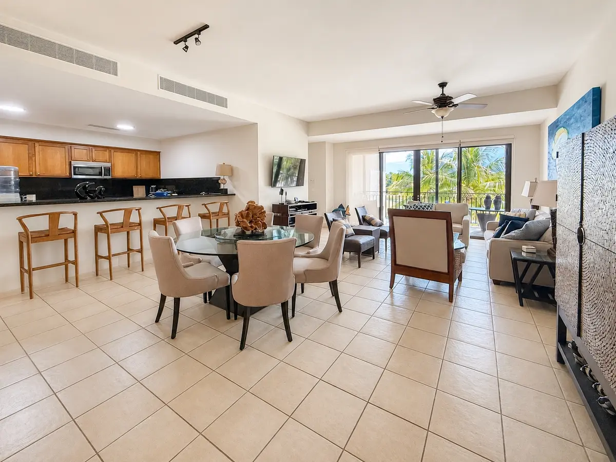 Sala y comedor abiertos del apartamento 623 en Paseo de las Casas, con mesa redonda de vidrio, barra de cocina con cuatro bancos de madera y puertas al balcón.
